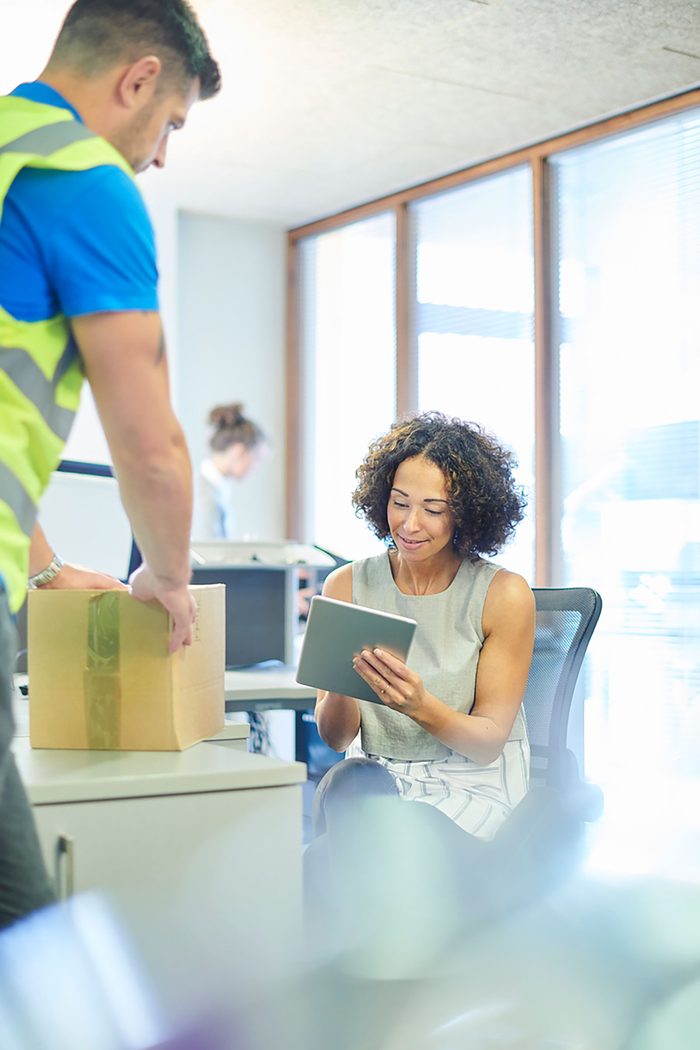 A courier delivering a box to a business owner working on a tablet