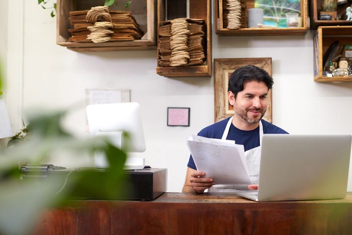 Business cash advance: a shop owner going over paperwork at his laptop behind the counter
