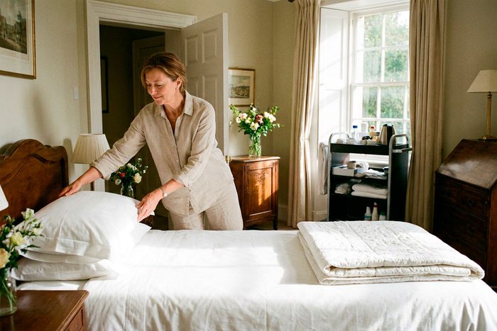 MCA funding for hotels: a hotel owner finishes making up a guest room in afternoon light, a housekeeping cart waiting in the corridor behind her.