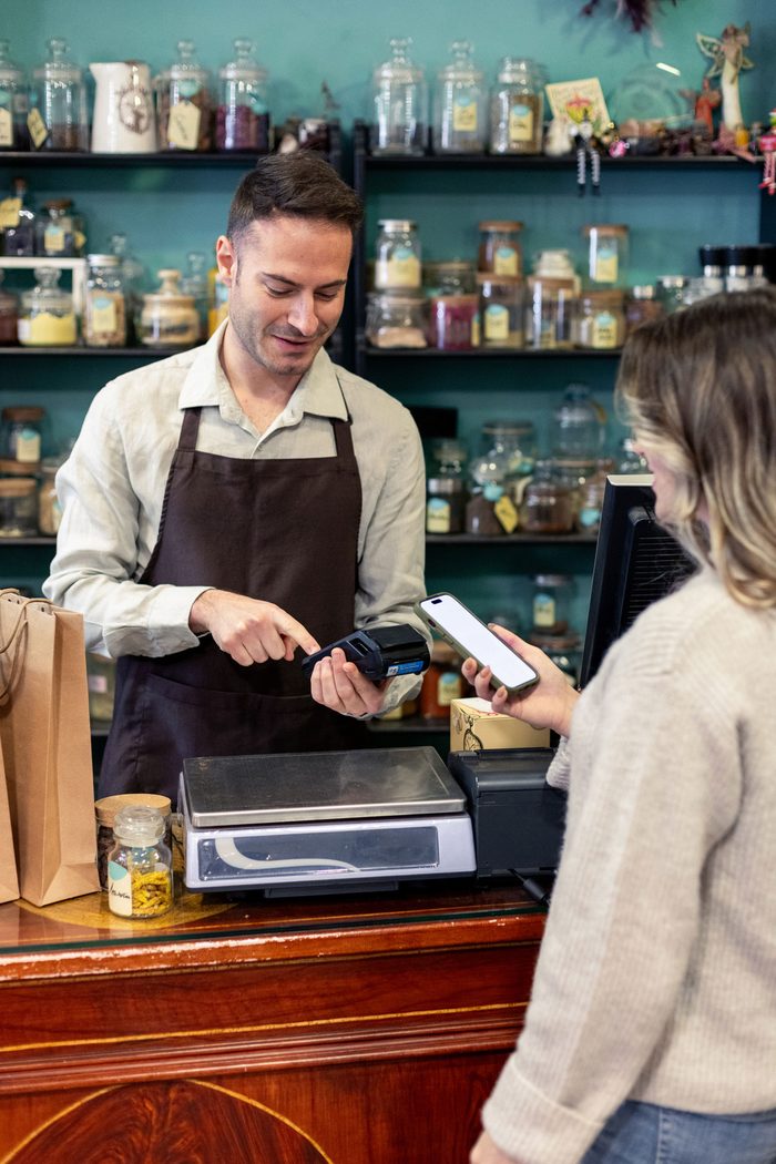 MCA financing: a shop owner taking a customer&rsquo;s phone payment at the counter