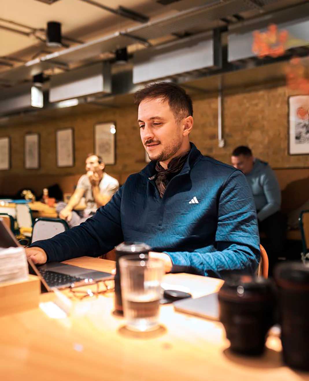 A Cardiff team member working at a laptop at a long shared table, colleagues at work behind them.